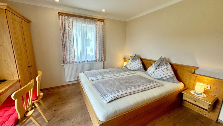 image00010, © Familie Buber A cozy bedroom with wooden furniture, a double bed, and a desk.