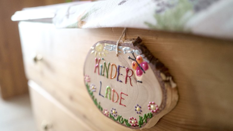 Kinderlade mit Büchern, Malsachen und Spiele, © Auftragsfoto.at Nahaufnahme eines Holzschildes mit der Aufschrift 'Kinderlade' an einer Kommode.