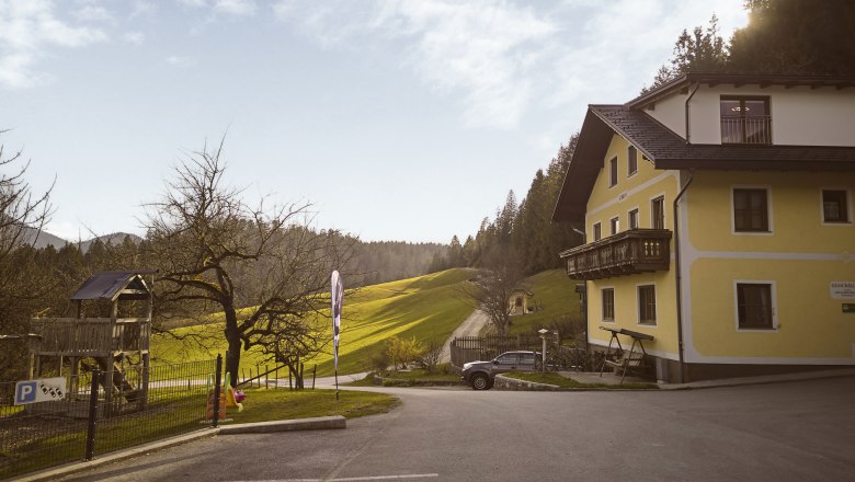 Familienbauernhof Glockriegl, © Auftragsfoto.at Der Familienbauernhof Glockriegl- ein gelbes Bauernhaus mit Balkon steht in einer grünen, hügeligen Landschaft.