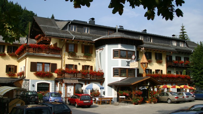Gasthof Kirchenwirt, © Tibor Borgyos Ein traditionelles Gasthaus mit blumengeschmückten Balkonen und geparkten Autos davor.