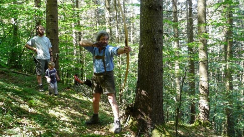 Archery Salzatal, © Bogensport Salzatal Person shoots with a bow in the forest, two other people in the background.