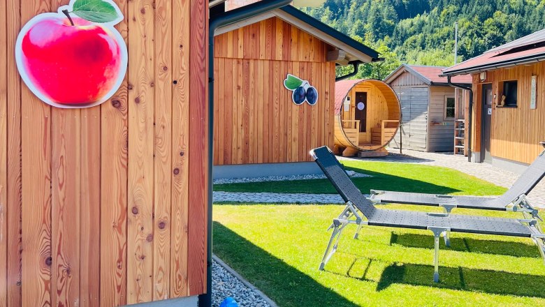Meine kleine Auszeit (c)Melanie Heim (2), © Melanie Heim Wooden cabins decorated with fruit and deck chairs on a meadow, surrounded by mountains.