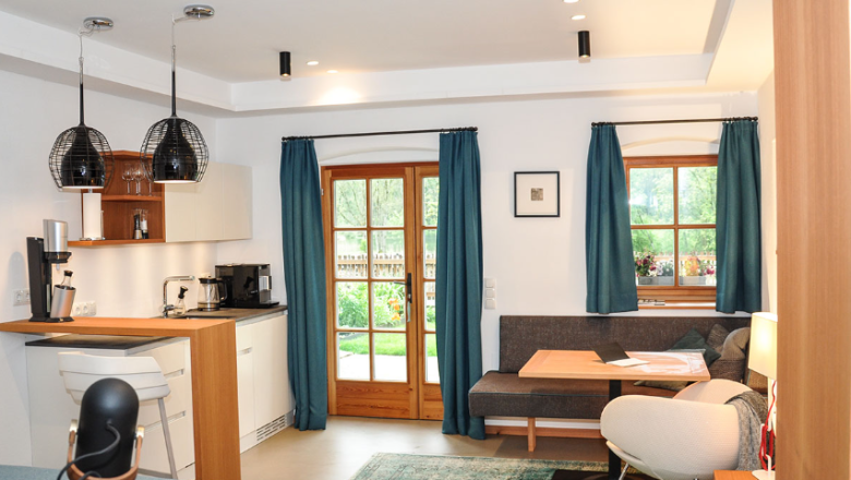 Das Studio ist ideal für zwei Personen und lädt zum gemütlichen Verweilen ein.
Auf der Terrasse genießt man mit Blick zum See sein Frühstück oder in den Abendstunden den Aperitif.
In der kleinen Küchenzeile ist der Salat für das Picknick am See schnell zubereitet.
Unter der Regendusche im offen gestalteten Bad kann man den Alltag hinter sich lassen., © Sophie Kirchner Modernes Studio-Apartment mit Küche, Esstisch und gemütlicher Sitzecke, Blick auf den Garten durch große Fenster.