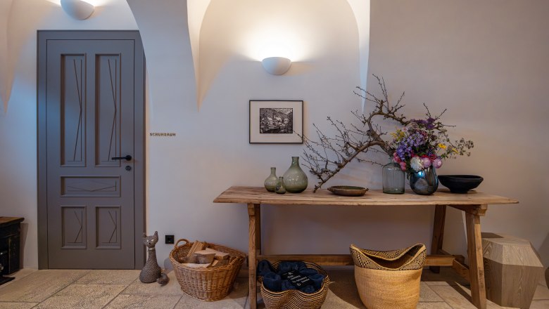 Refugium Lunz, © Niederösterreich Werbung / Maximilian Pawlikowsky Innenraum mit Holztisch, Vasen, Blumen und Körben. Tür mit Aufschrift 'Schuhraum'.