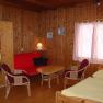 Ferienhäuser Kogelsbach, © Ferienhäuser Kogelsbach Innenansicht eines gemütlichen Zimmers mit Holzwänden, rotem Sofa, Tisch, Stühlen und Bett.