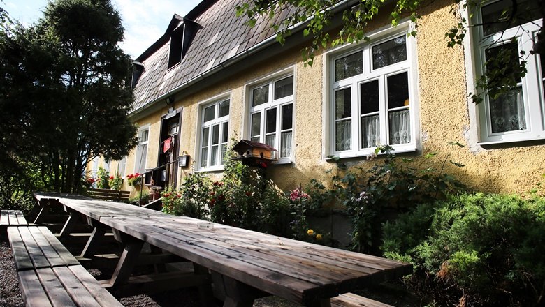 Snack station "Alte Schule", © Wein Franz Yellow building with white windows and long wooden benches in the foreground.