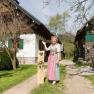 Hanni's color barn, © Hanni Reichlin A woman in traditional dress stands in front of two rustic buildings in a green courtyard.