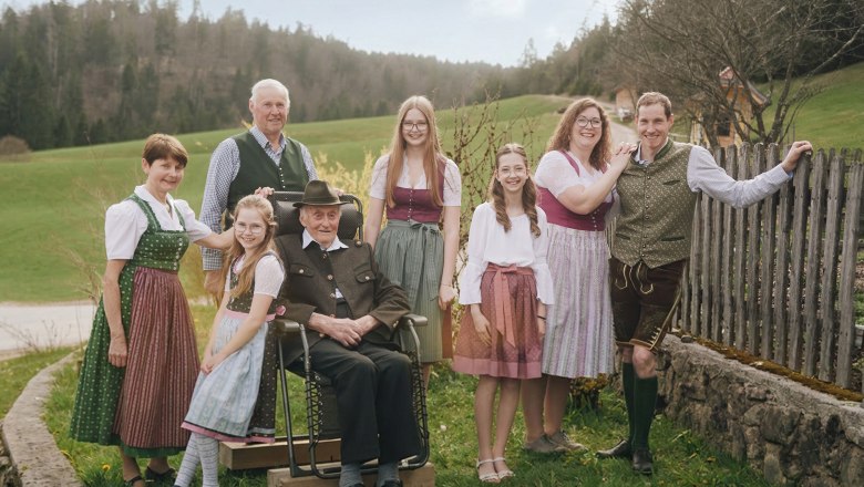 Familie Grasberger, © Auftragsfoto.at Eine Familie in traditioneller Tracht posiert im Freien vor einer ländlichen Kulisse mit Wiesen und Bäumen.
