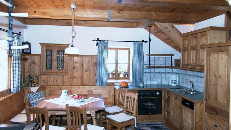Küche, © Ferienhaus Hintereck Rustikale Küche mit Holzmöbeln, Esstisch und Stühlen, Herd, Spüle und Fenster mit karierten Vorhängen.