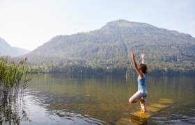 Yoga mit der Gastgeberin Manu vom Haus am See, © Familie Mayr Eine Frau macht Yoga in einem See mit einem Berg im Hintergrund.