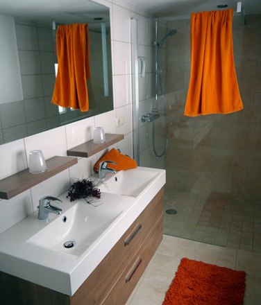 Vacation home Eva Deufl - Apartment Heuboden - Bathroom, © Ferienhaus Eva Deufl Modern bathroom with double washbasin, large mirror, shower and orange accents.