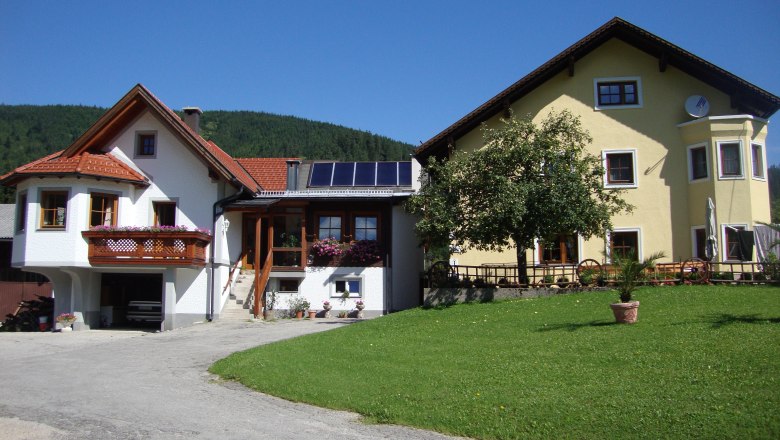 Heike and Arthur Schlögelhofer, © Heike Schlögelhofer Two houses with a garden and flowering plants, blue sky in the background.