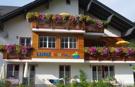 Lunzferien Geli Mayr, © zVg Ein Ferienhaus mit bunten Blumen auf den Balkonen und dem Schriftzug 'LUNZ Ferien'.