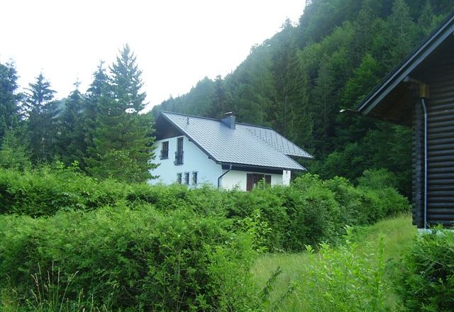 Eingebettet in Wald und Wiesen: das Haus Hager, © zVg Ein weißes Haus mit grauem Dach, umgeben von grünen Büschen und Bäumen, in einer ländlichen Waldlandschaft.