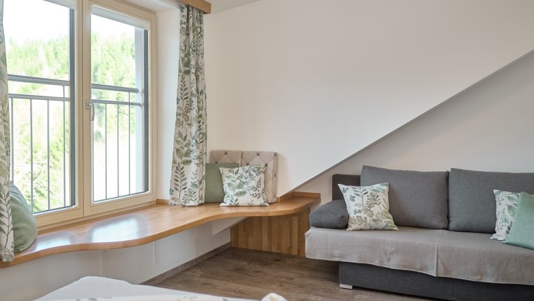 Stallgucker-Wohnung 2 - Schlafzimmer mit Stallguckerfenster, © Auftragsfoto.at Wohnzimmer mit großem Fenster, grauem Sofa und Holzboden.