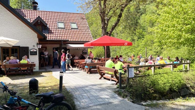 Schindlhütte im Sommer, © Andreas Rasch Eine Berghütte mit Terrasse, auf der Menschen an Tischen sitzen. Fahrräder sind im Vordergrund zu sehen, umgeben von grüner Natur.