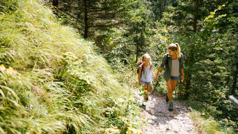 Hiking, family, Trefflingfall, Ötscher Tormäuer Nature Park, Mostviertel, © Niederösterreich Werbung/Andreas Jakwerth A mother and daughter walk happily along a narrow path surrounded by lush greenery and tall trees. The fresh air and the gentle babbling of a nearby stream create an inviting atmosphere for families who want to explore nature.