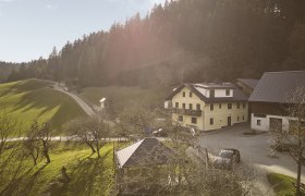 Glockriegl_@Auftragsfoto-at_DJI_0049-web, © Auftragsfoto.at A farm in a rural setting with green meadows and a forest in the background.