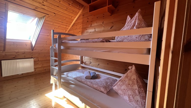 Ferienwohnung am Biohof Herdengl, © Ybbstaler Alpen_Karin Hager Ein gemütliches Schlafzimmer mit Holzverkleidung und einem Etagenbett unter einem Dachfenster.