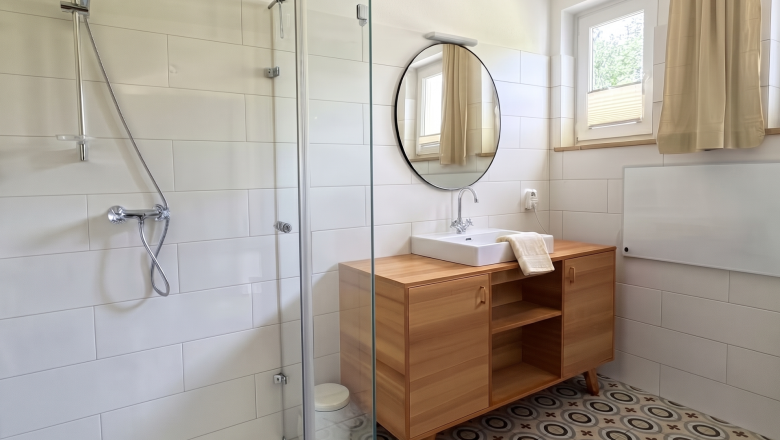 Magda Bathroom, © Raphaela Bachler Modern bathroom with a shower, sink, and wooden cabinet.