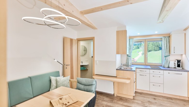 Kuschelapartment 3 - Wohnen, © grasberger Modernes Apartment mit Holzelementen, Küchenzeile und Esstisch. Fenster mit Blick auf grüne Landschaft.