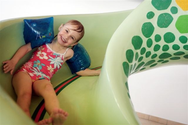 Ybbstal brine bath, © Ybbstaler Solebad A laughing child with water wings slides down a green water slide.