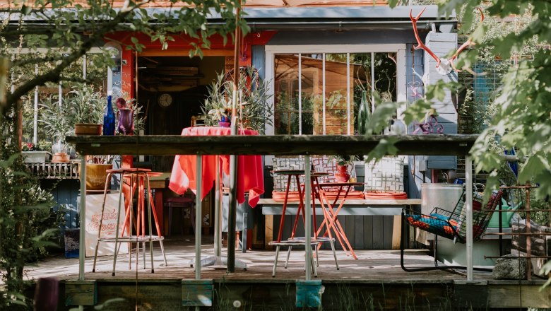 The workshop, image & project workshop, © Foto Hochenauer Colorful terrace in front of the location with red chairs and table, surrounded by plants and decorations.