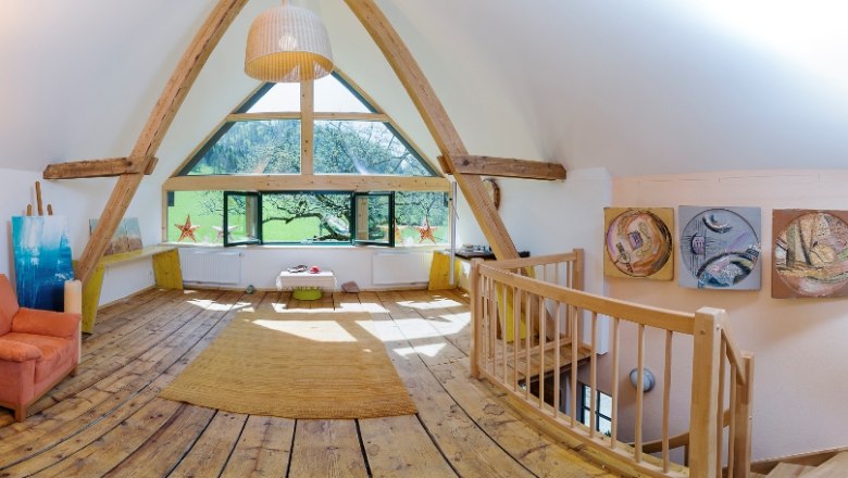 Interior view of an attic with wooden floor, large windows and works of art on the walls.
