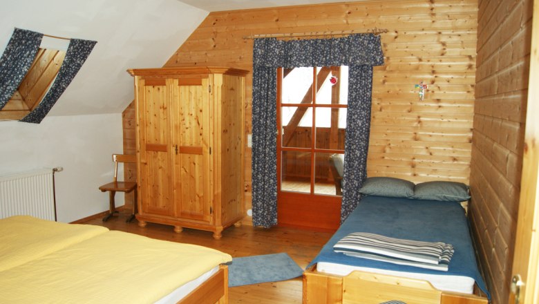 Interior view of a rustic bedroom with wooden walls, a double bed, a single bed and a closet.