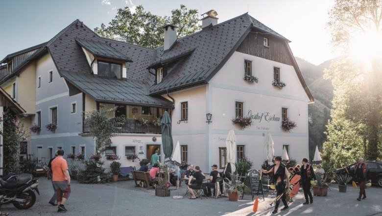 Ein traditionelles Gasthaus mit Menschen im Freien bei Sonnenschein.