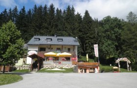 Ein Restaurant mit Terrasse und Sonnenschirmen vor einem Wald.