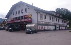 Building with Spar-Lengauer supermarket and Post-Partner sign, cars and bicycles in front of it.
