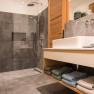 Modernes Badezimmer mit grauen Fliesen, Glasdusche und Holzwaschtisch.