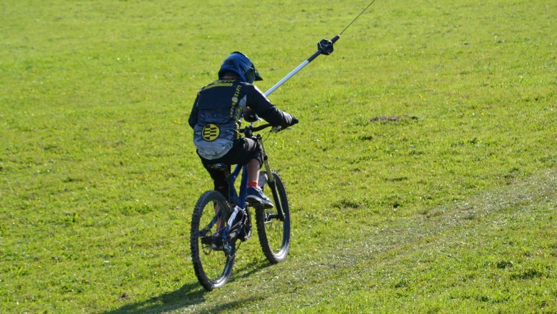 A mountain biker is pulled along a green meadow by a drag lift.