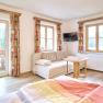 Helles Zimmer mit Sofa, Tisch, Fernseher und Balkon mit Waldblick.