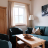 A cozy living room with green upholstered furniture, a wooden table, and a window with curtains.