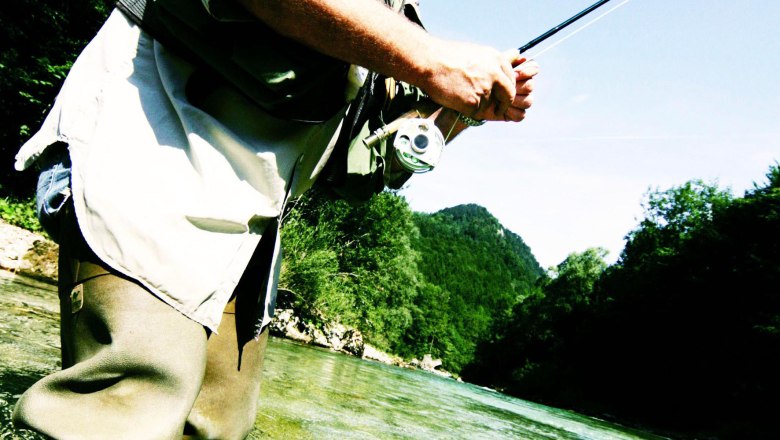 A man fly fishing in a river, with a jumping fish in the foreground.