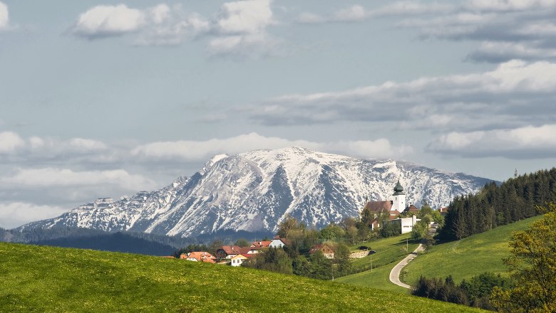 View of St. Leonhard am Walde with a snow-covered mountain in the background.