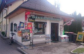 Exterior view of a small tobacco store with advertising signs and newspaper stands.