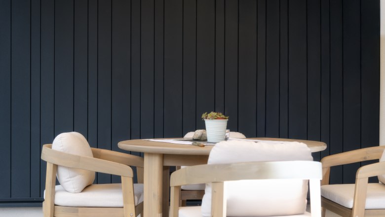 Ein runder Holztisch mit vier gepolsterten St&uuml;hlen vor einer dunkelgrauen Wand.