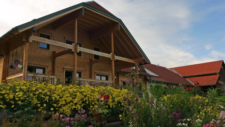 A traditional farmhouse with wooden cladding and a flowering garden in the foreground.