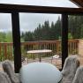 Blick von einem Innenraum auf eine Holzterrasse mit Wald im Hintergrund.
