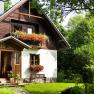 Ein malerisches Ferienhaus mit Holzverkleidung und Blumenk&auml;sten, umgeben von &uuml;ppigem Gr&uuml;n.
