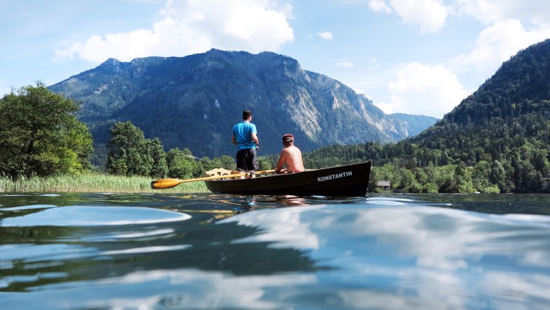 Two people in a boat on a lake, surrounded by mountains and trees.