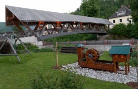 Covered wooden bridge over a river with a small water wheel in the foreground.