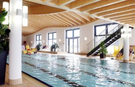 Interior view of a swimming pool with wooden ceiling and large windows.