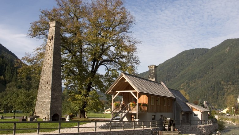 Historisches Gebäude mit Schornstein und Wasserrad in ländlicher Umgebung.