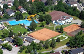 Luftaufnahme eines Freibads mit Schwimmbecken, Rutsche und Tennisplätzen in einer Wohngegend.