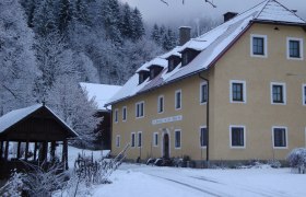 A yellow building in the snow, surrounded by snow-covered trees and a wooden pavilion.