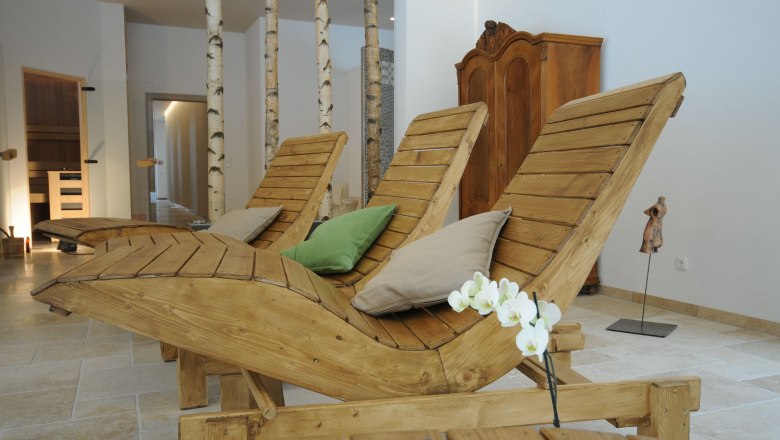Innenansicht eines Wellnessbereichs mit Holzliegen, Kissen und Birkenstämmen.